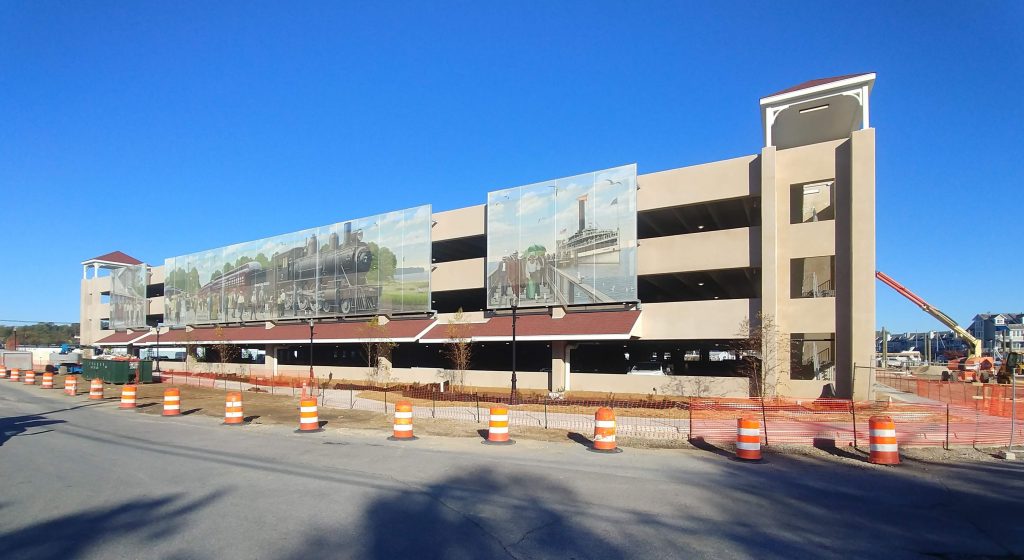 Exterior of parking structure under construction showing large murals attached to facade