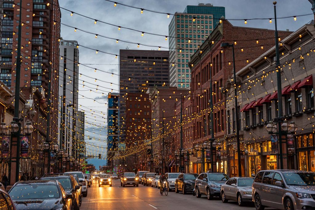 An inviting downtown street in the evening with lights strung above the road and lots of activity