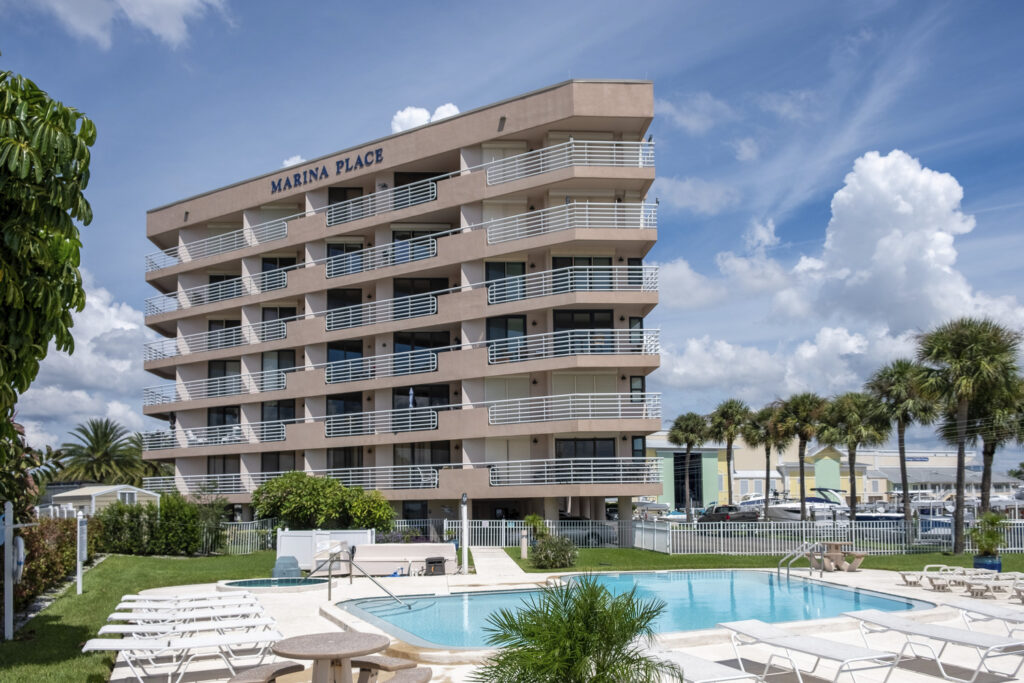 Marina Place Condominium, a pink stucco mid-rise building, with sunny blue skies and pool in the foreground