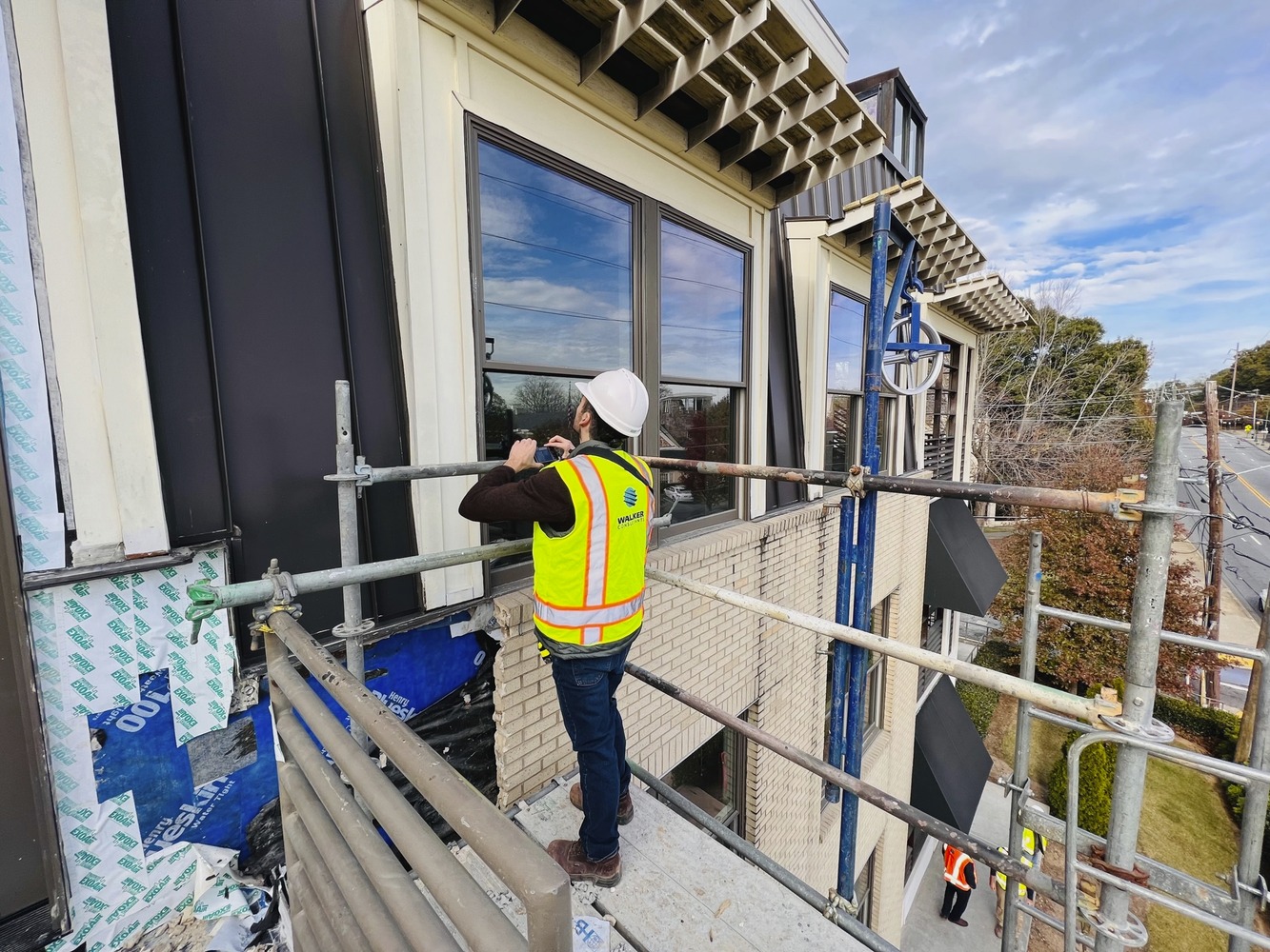 A person in a hard hat and Walker Consultants neon vest takes a photo of work occurring on a building facade